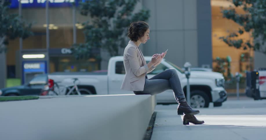 Woman checking her smartphone sitting on a bench on a street in the city