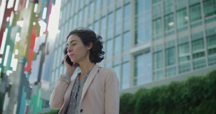 A woman talks on her phone while standing outside an office building in a city