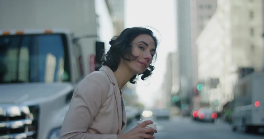 A woman looks down a busy city street with traffic while holding a coffee cup during the day