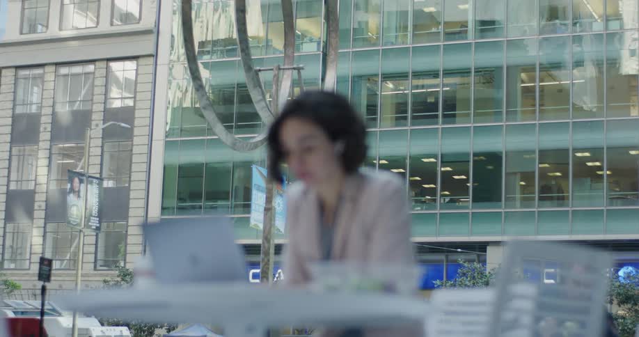 A woman is sitting down with food looking at her laptop outside