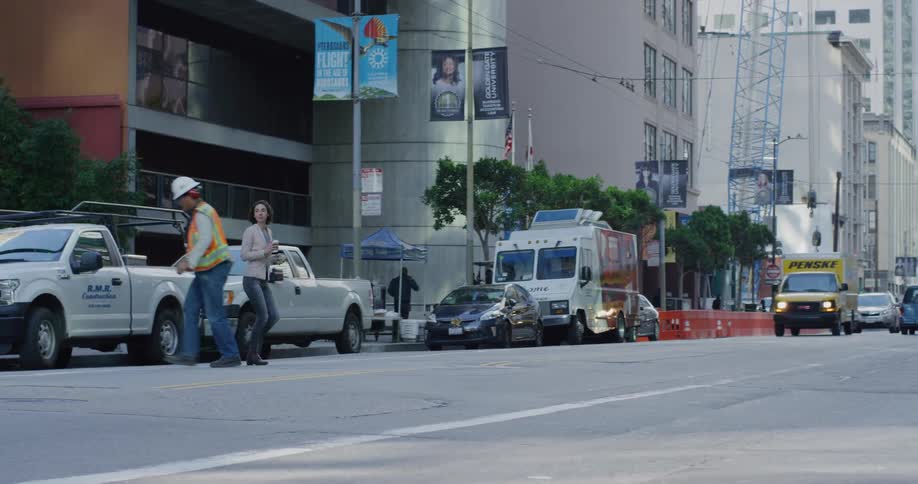 Woman and a construction worker crossing a busy street in downtown la at daytime