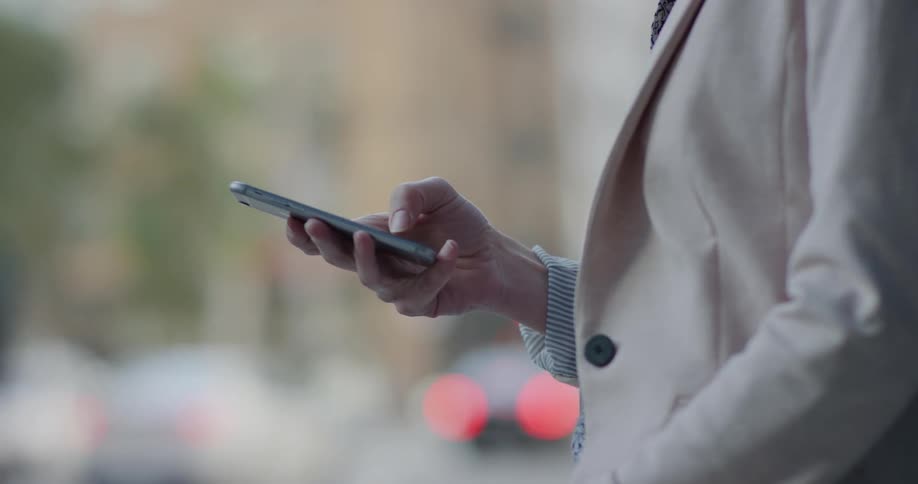Woman uses a smartphone while standing on a street in the city