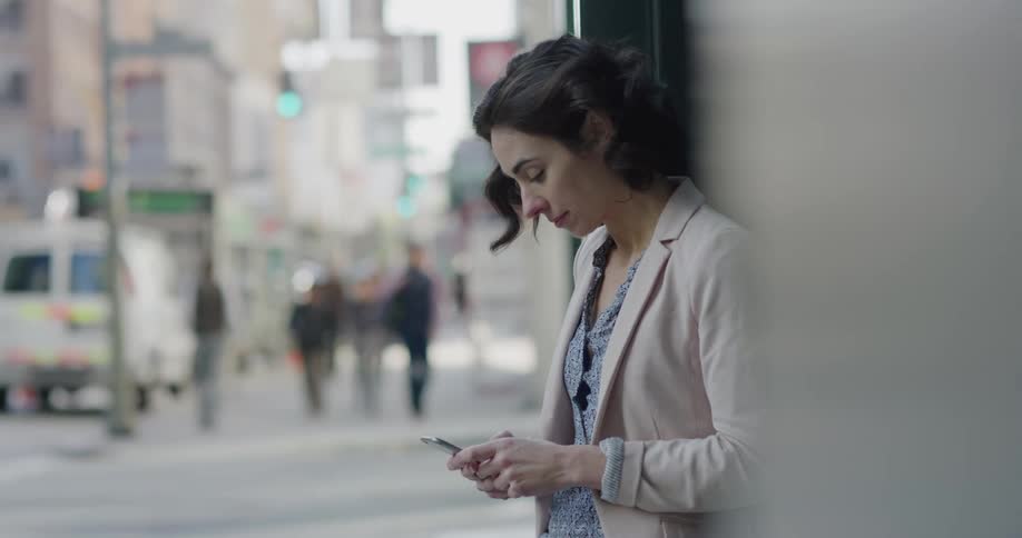 Woman checking her smartphone reclined on a building in a city street
