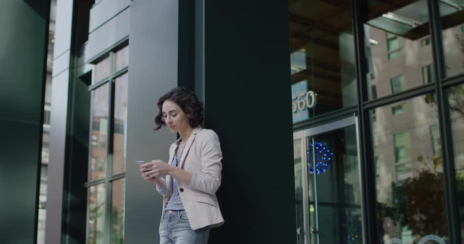 Young woman texting on her smartphone reclined on a building in the citys downtown