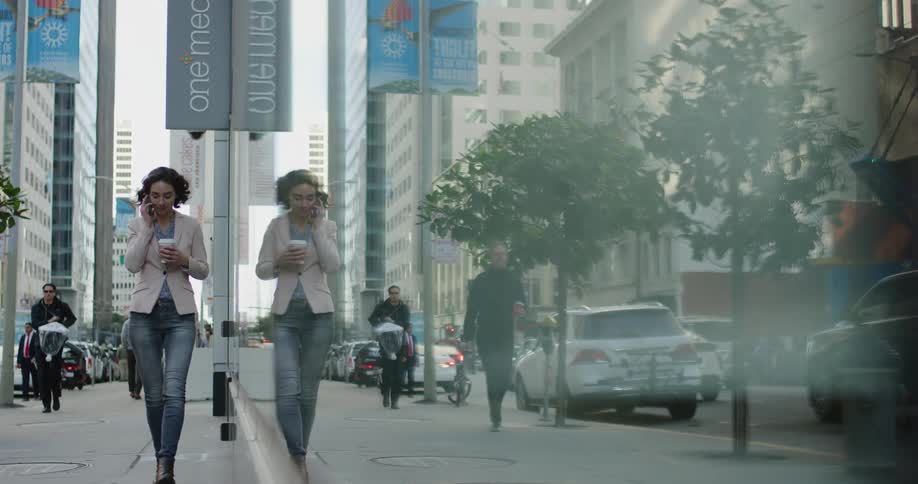 Young woman talking on her smartphone and drinking coffee walks on the city street