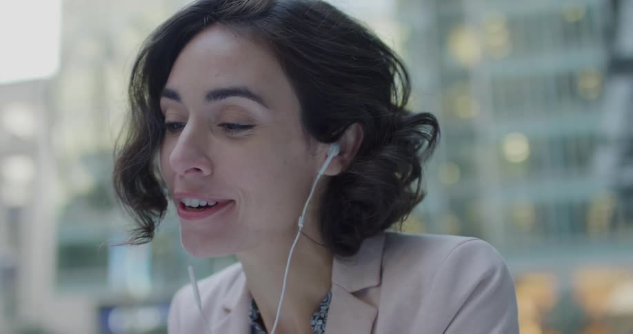 Young woman wearing earbuds smiles while taking a call on her smartphone
