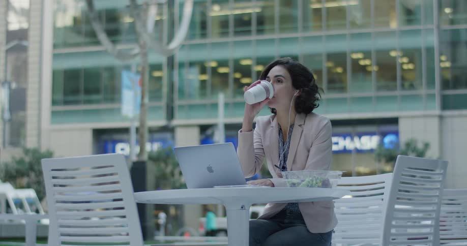 Woman drinking coffee on an outdoors cafe in the city downtown using a laptop