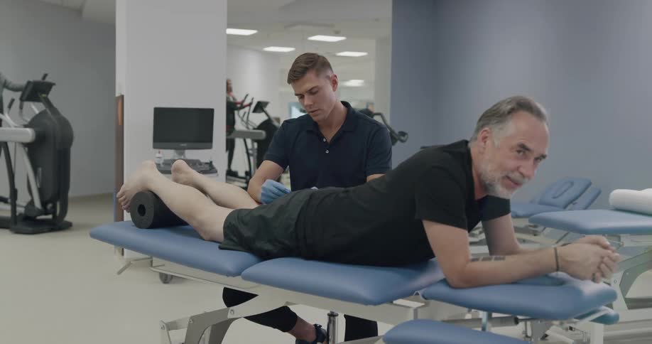 A man lies on a table and receives acupuncture in a physical therapy facility