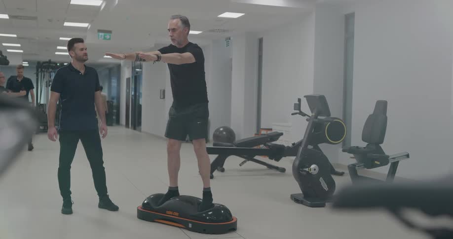 Trainer guides a man on fitness rehabilitation inside a gym
