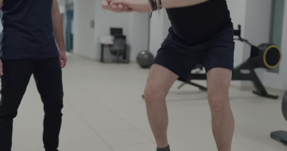 A trainer watches as his client does a squat while standing on a balance board
