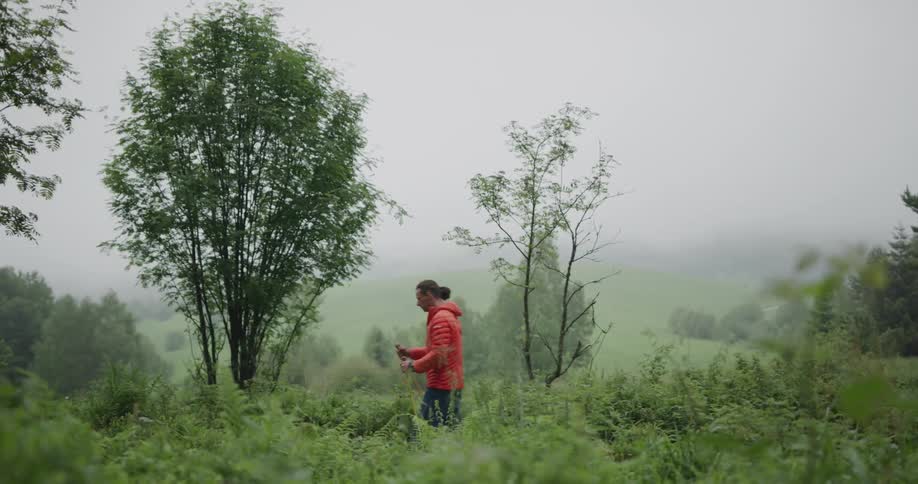 Man wearing red jacket hikes on a trail in the fields using walking sticks