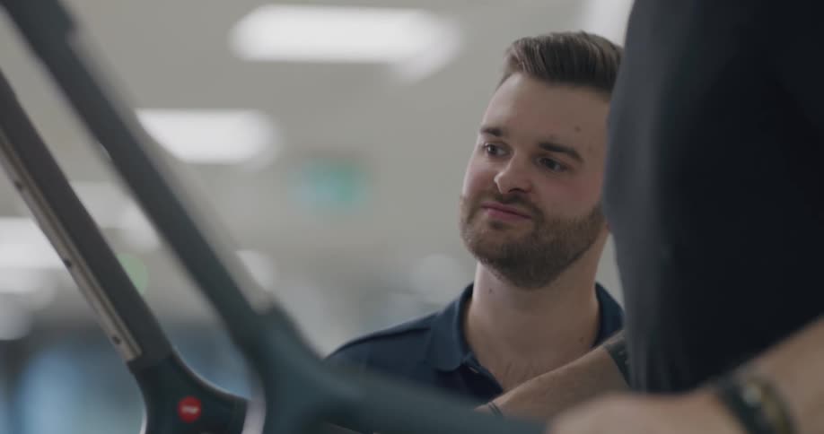 A man watches and points at a machine as a man exercises on it