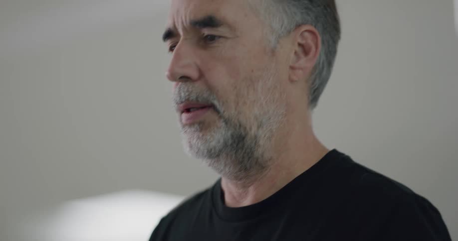 A man with a beard and wearing a black t shirt moves up and down indoors