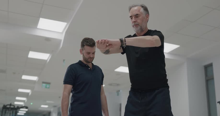 Trainer supervising a senior citizen doing rehabilitation exercises on a gym