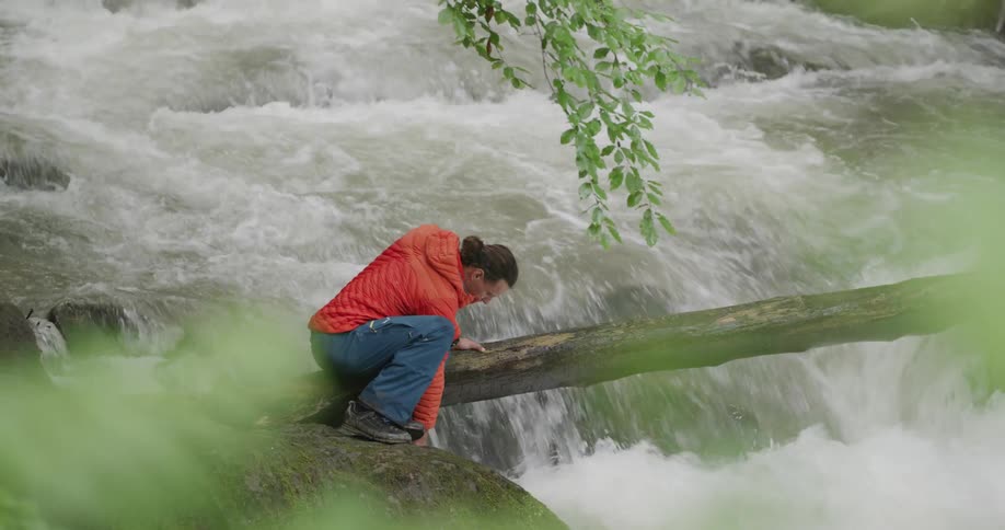 Man wearing orange hoodie is at the edge of a cliff watching the waterfall below