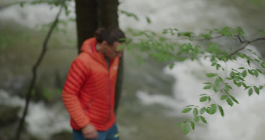 A man hiking next to river rapids holds on to trees as he walks