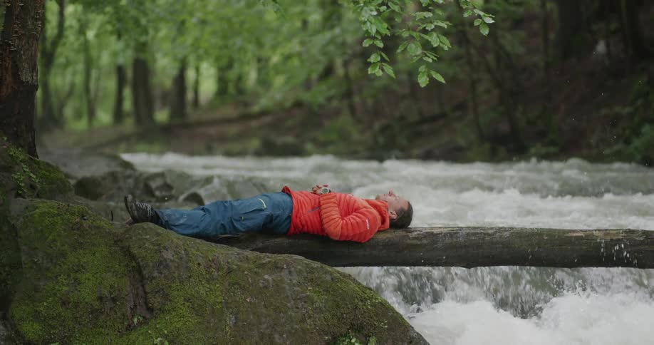 A man is resting on a log over the stream