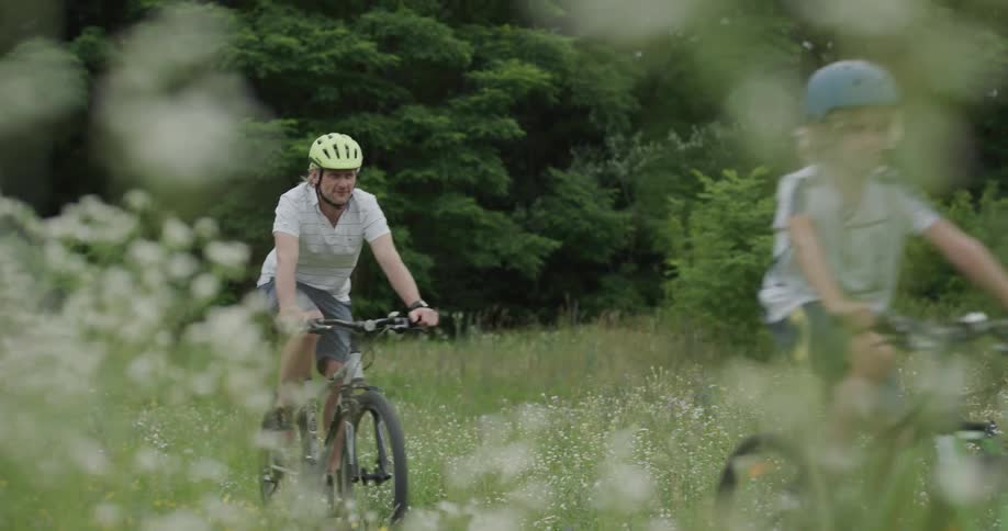 A father and son ride their bicycles on the field