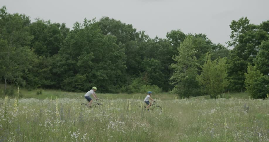 Father and son riding bicycles through the grass field near the forest at day time
