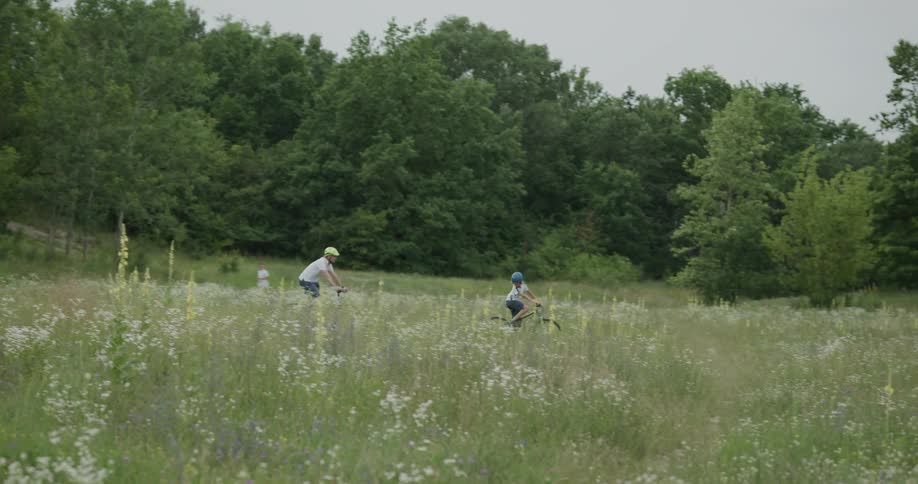 A man and boy wearing helmets ride bikes in a field surrounded by trees during the day