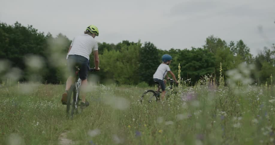 A father and his son bike through a field with wild flowers