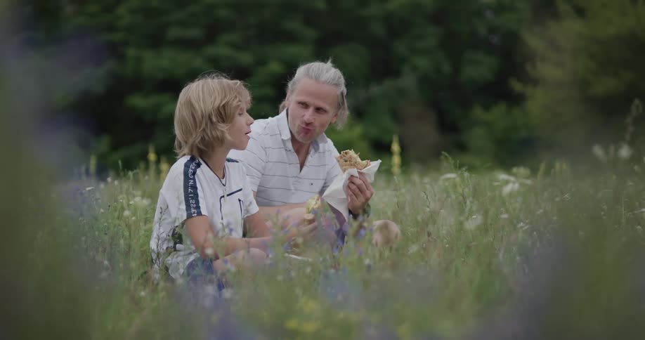 A man and boy are eating on the field