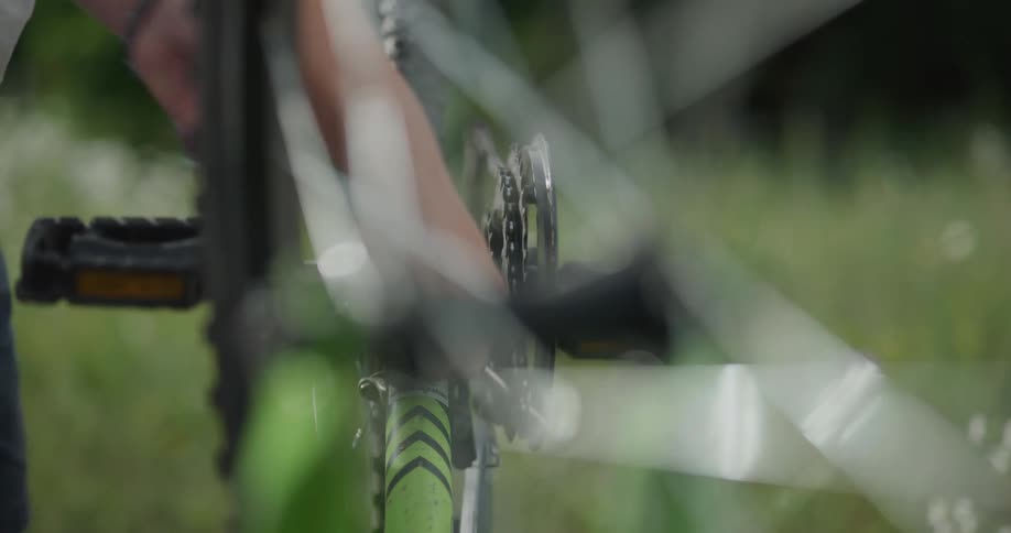 A person with a tool fixing a bike with grass and people in the background