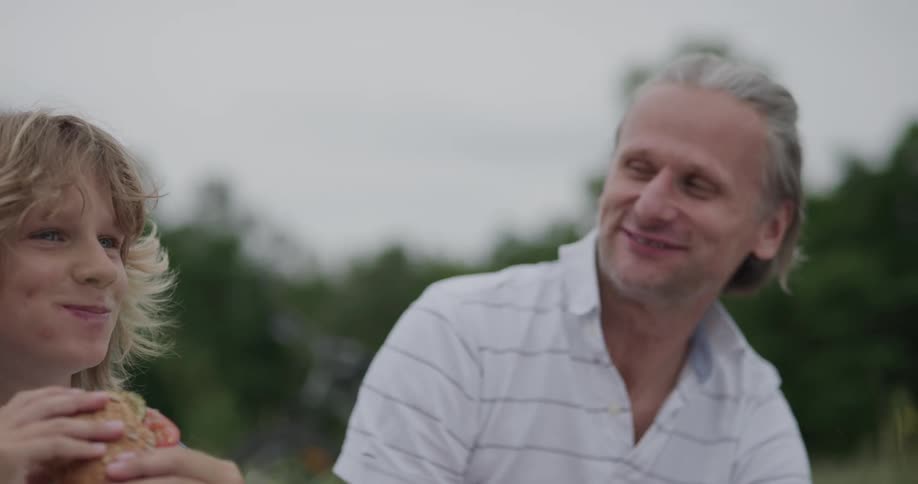 Father and son eating a sandwich enjoying lunch outdoors in nature