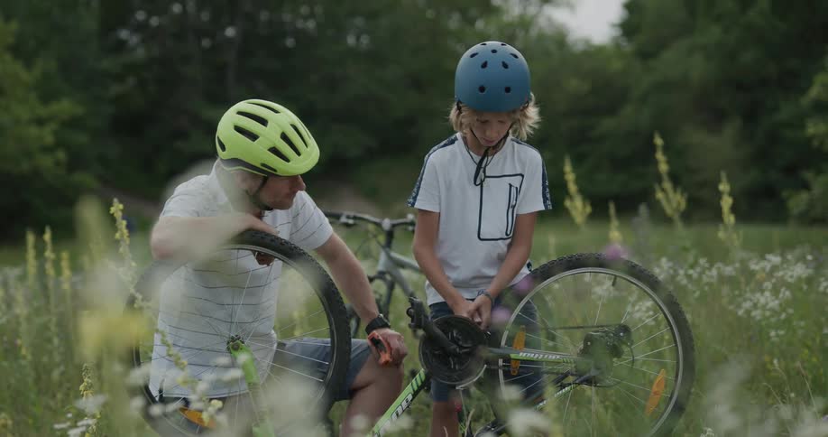 Father teaching son how to repair a bicycle in a grass field