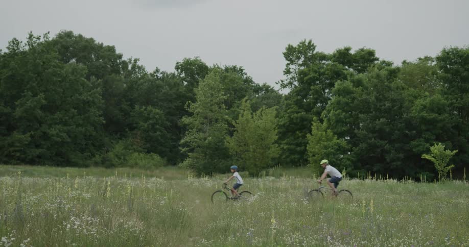 Father and son riding bikes on a trail through a grass field with a forest in the distance