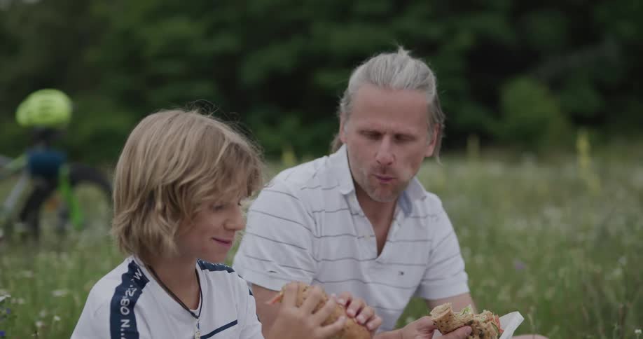 Father and son sharing sandwiches on the green grass in a field