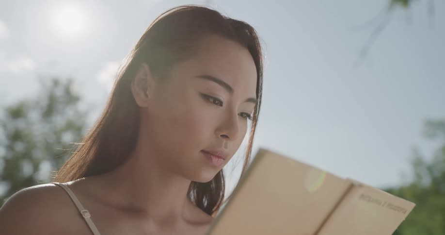 A young woman reads a book while outdoors on a sunny day