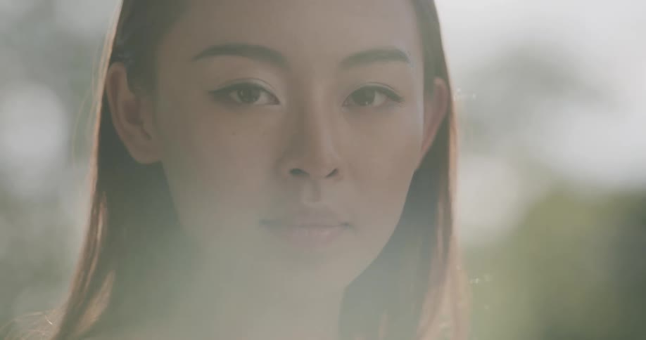 Close up of a young womans face looking at the camera standing outdoors at sunset
