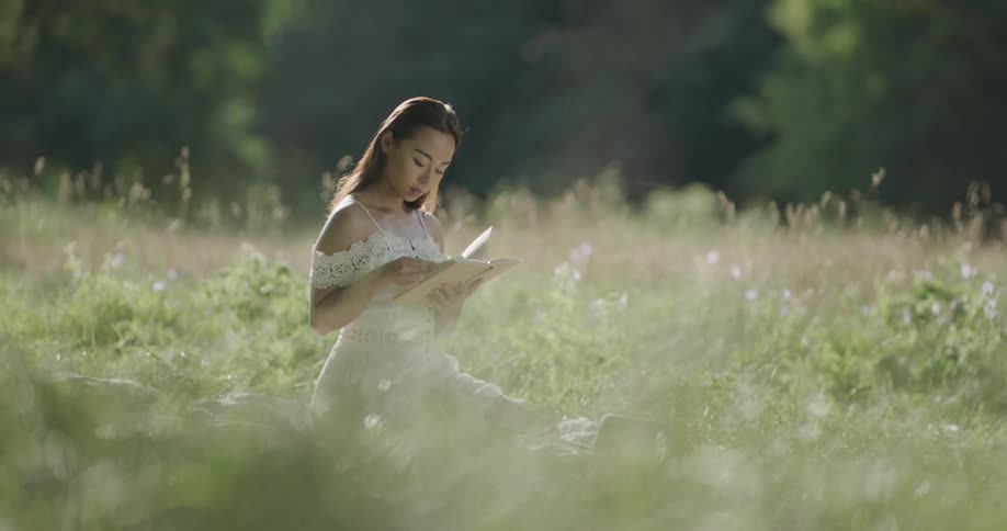 A woman sits outside on a field reading a book in the sunshine