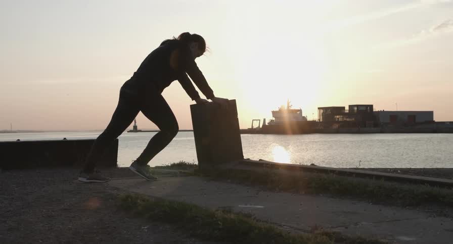 A woman is stretching near the water at sunset
