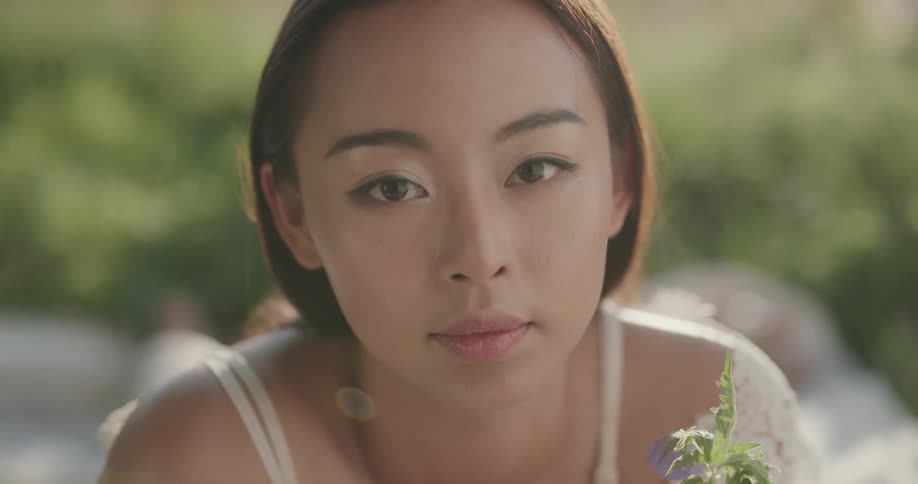 A woman wearing a white dress sits outside with a flower in her hand