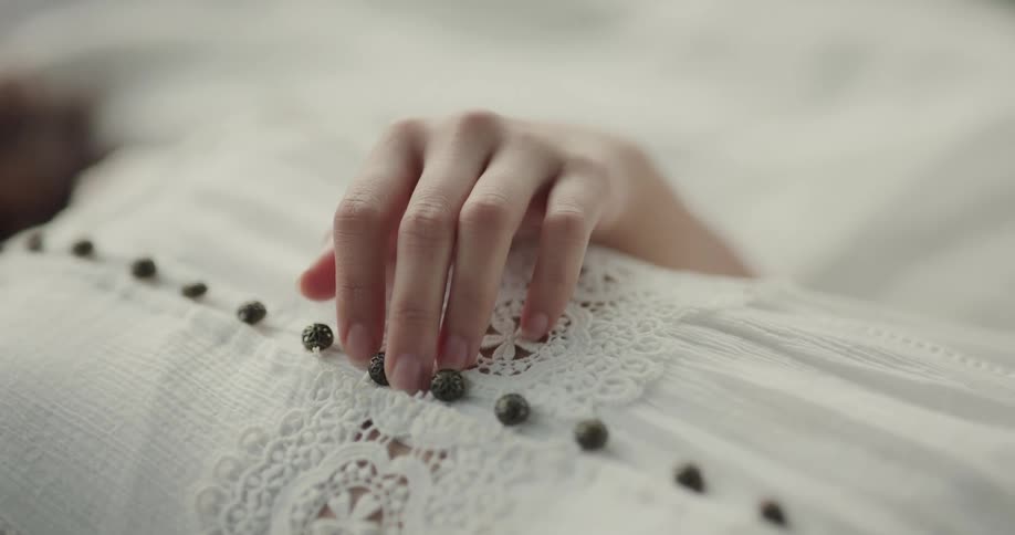 Hand laying over the dress in the chest of a woman over a blanket
