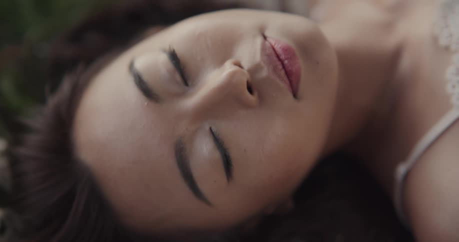 Woman wearing a lacey garment and laying on a striped blanket smiles and blinks her eyes