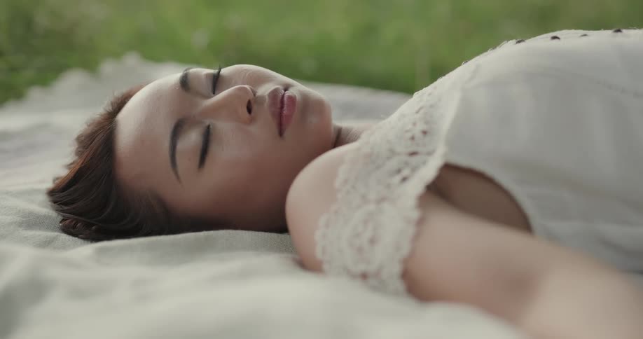 Woman with brown hair and white blouse lies on outdoor rug on grass in park