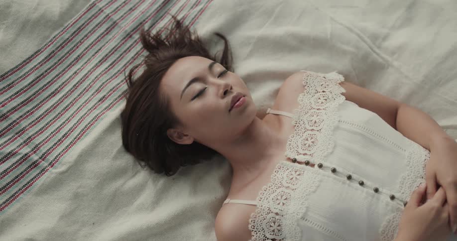 A woman laying down on a blanket on grass with her eyes closed