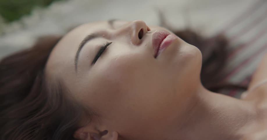Woman with brown hair and white blouse lies on outdoor rug on grass in park