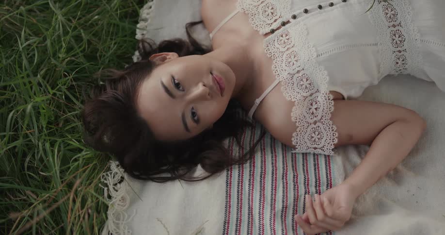 A woman in white dress with lace trim wakes from sleeping on a blanket in the grass and smiles