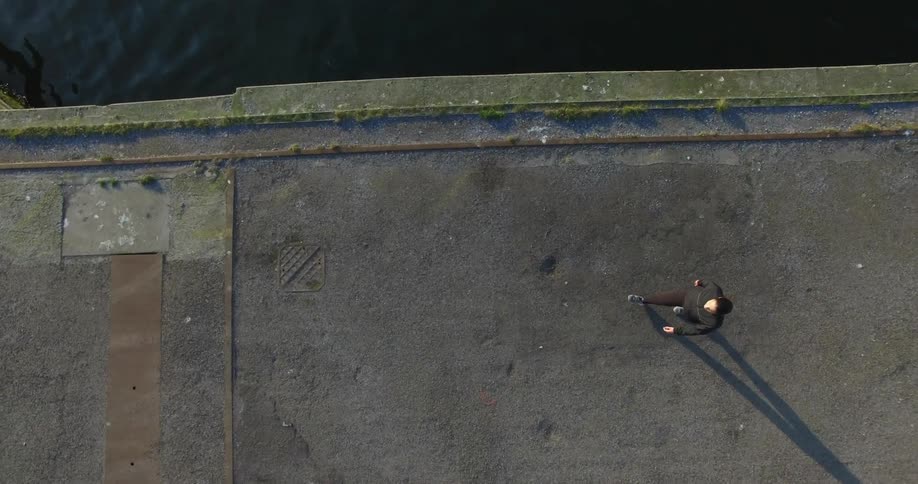 A man walking on a bridge over water being filmed from above