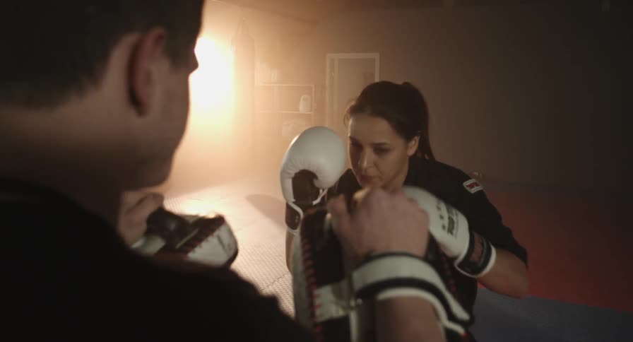 A female boxer practices punches in a gym with a trainer