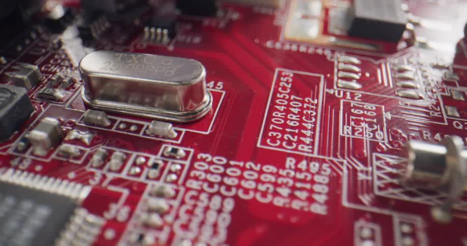 A red circuit board has metal and black components with white letters and numbers