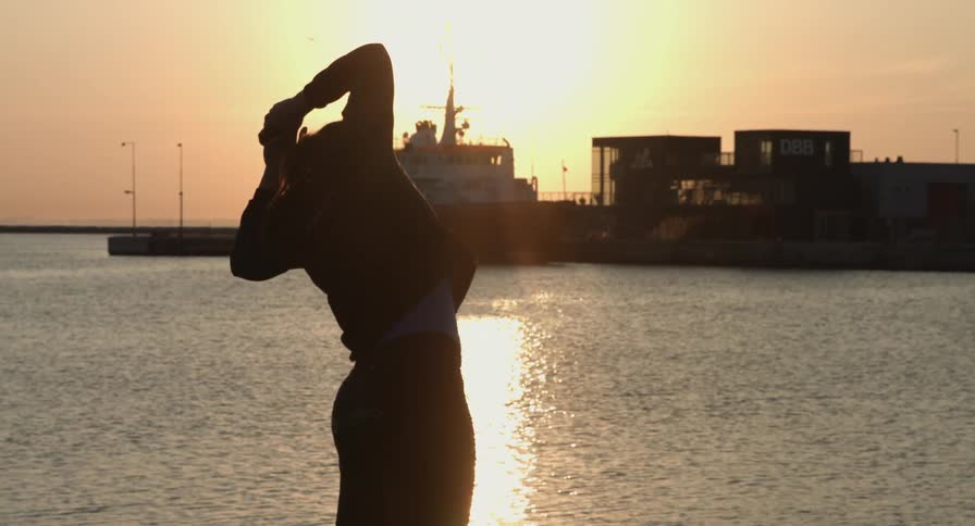 Woman stretching at dawn near an ocean pier