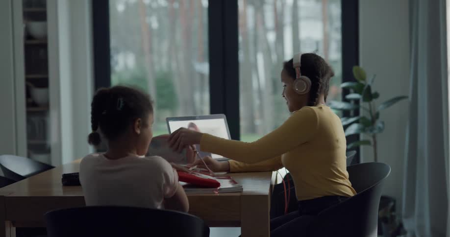 Two sisters sitting down at a table at home to do online school
