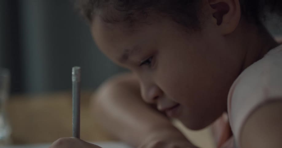 A girl in a room at a table with a pencil drawing on a book