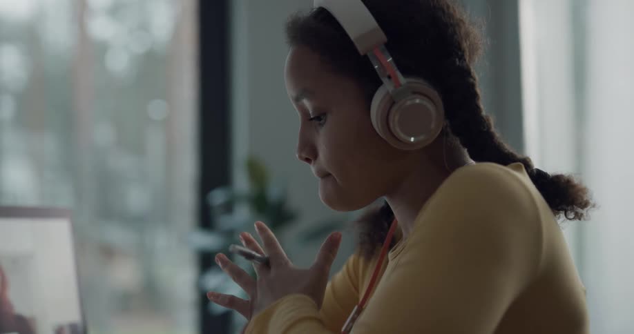 Girl wearing headphones takes online classes on a laptop at home