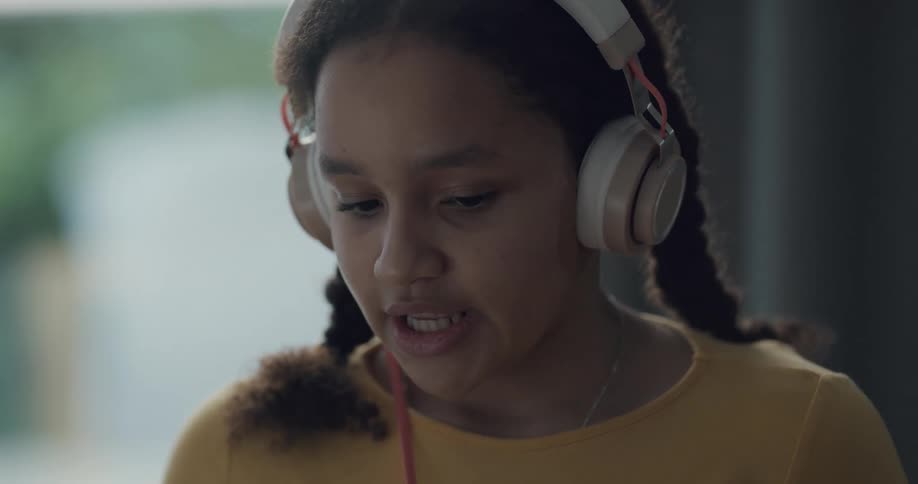 A young girl reads aloud while wearing headphones